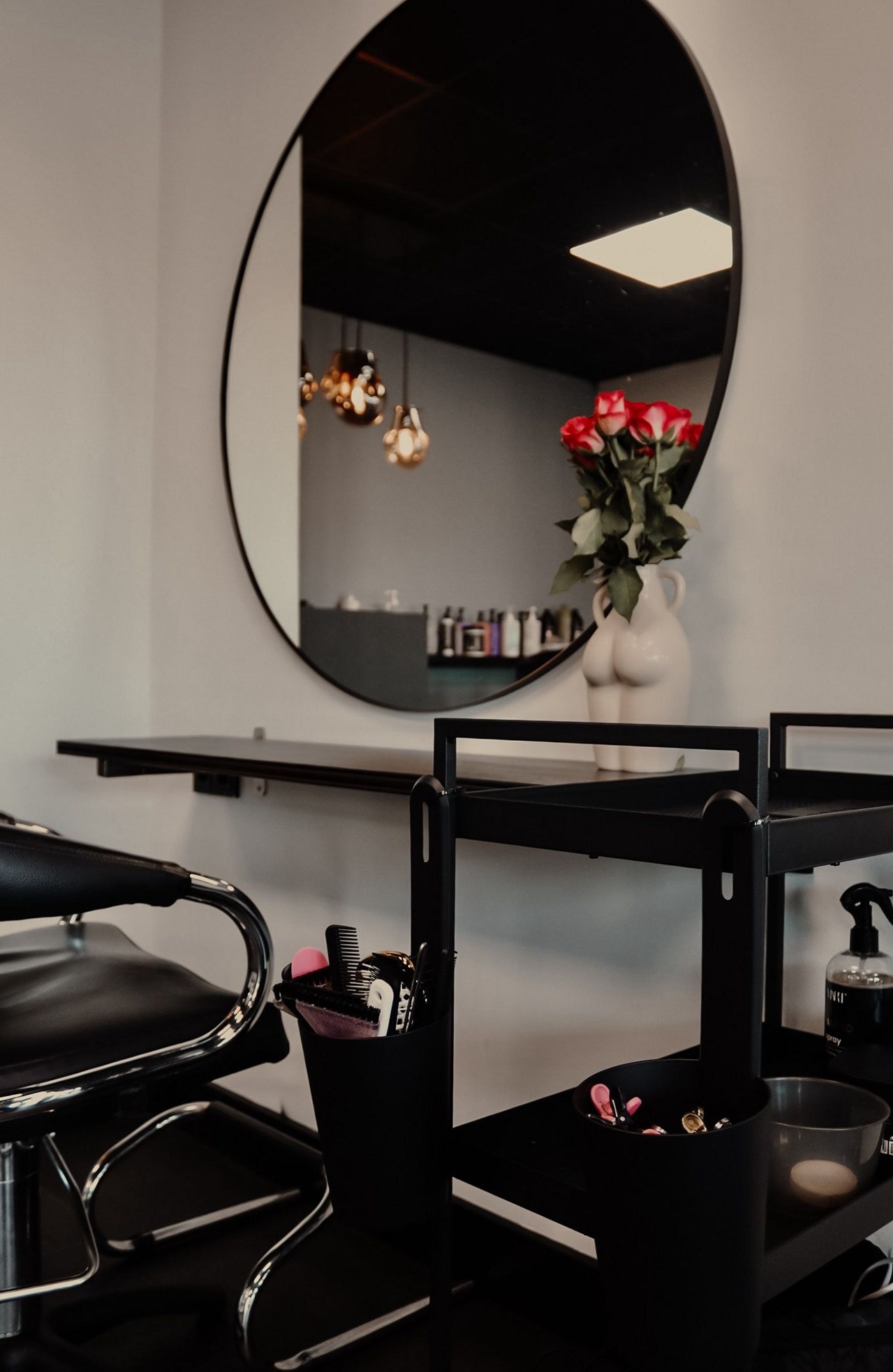 Een kapstation met een grote ronde zwarte spiegel, een zwarte trolley en rode tulpen