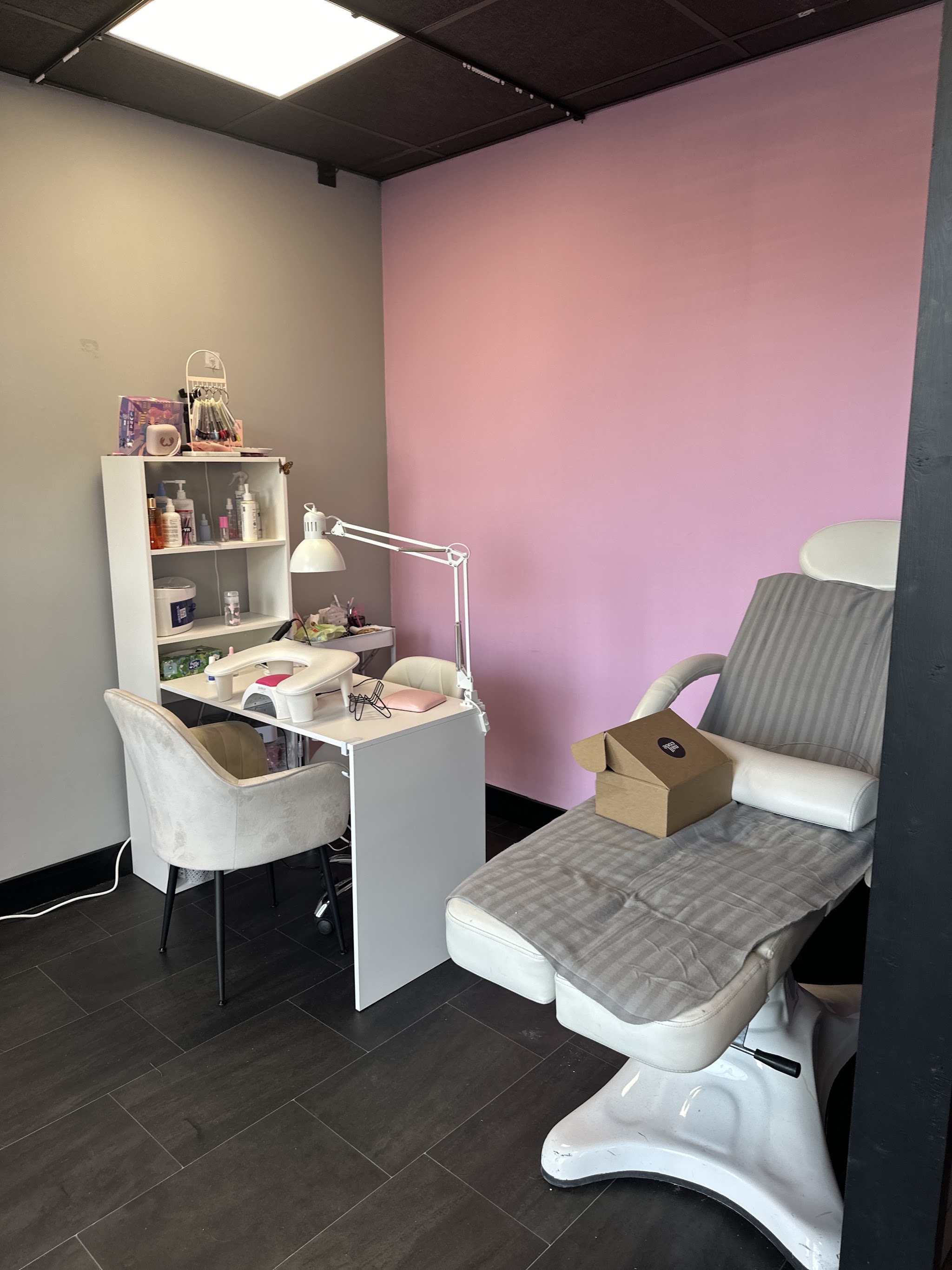 De behandelhoek met roze wand, manicuretafel met uv-lamp en een grijze behandelstoel