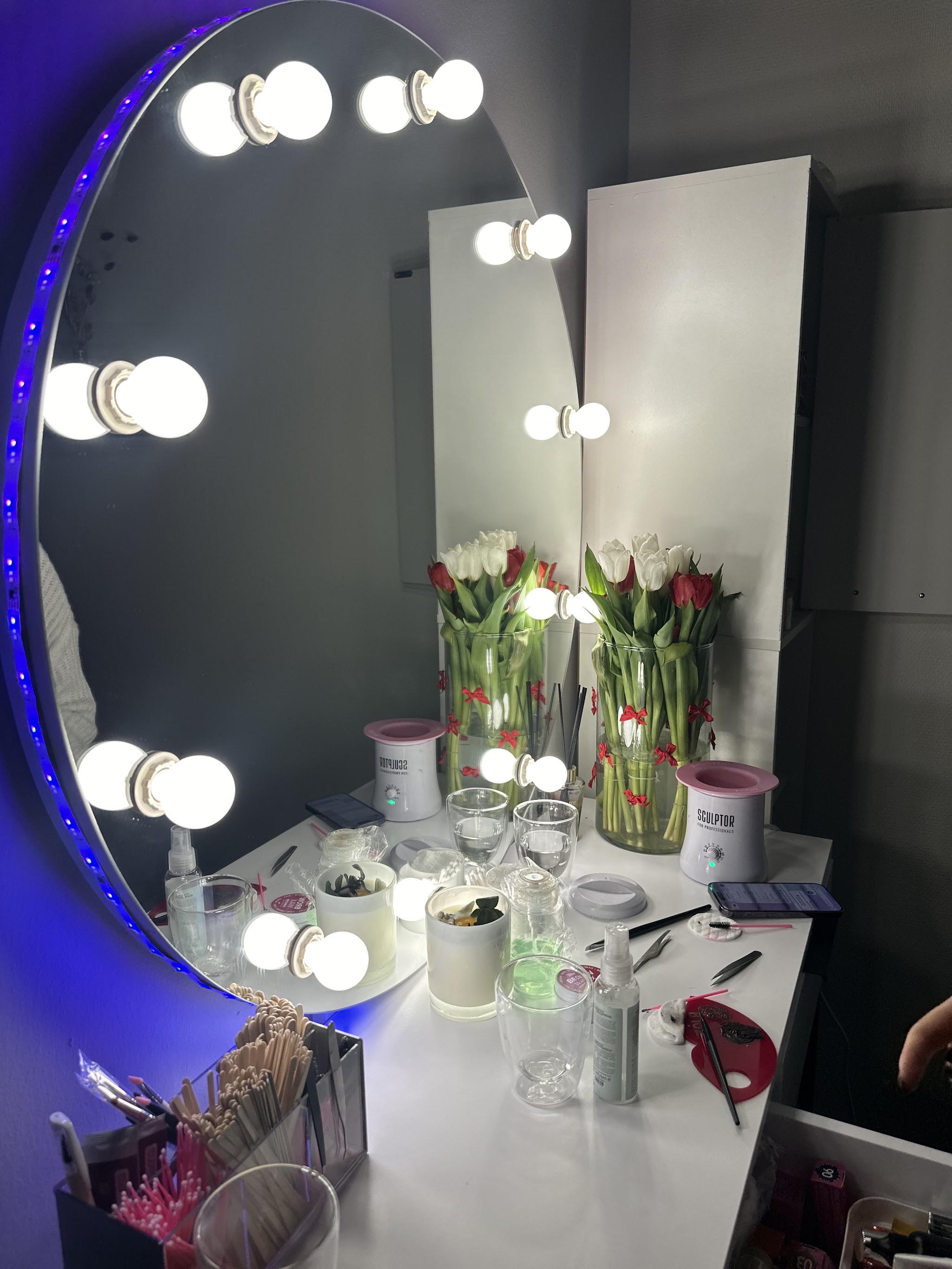 Visagietafel met een spiegel met lampen, een paarse ledrand en een vaas tulpen