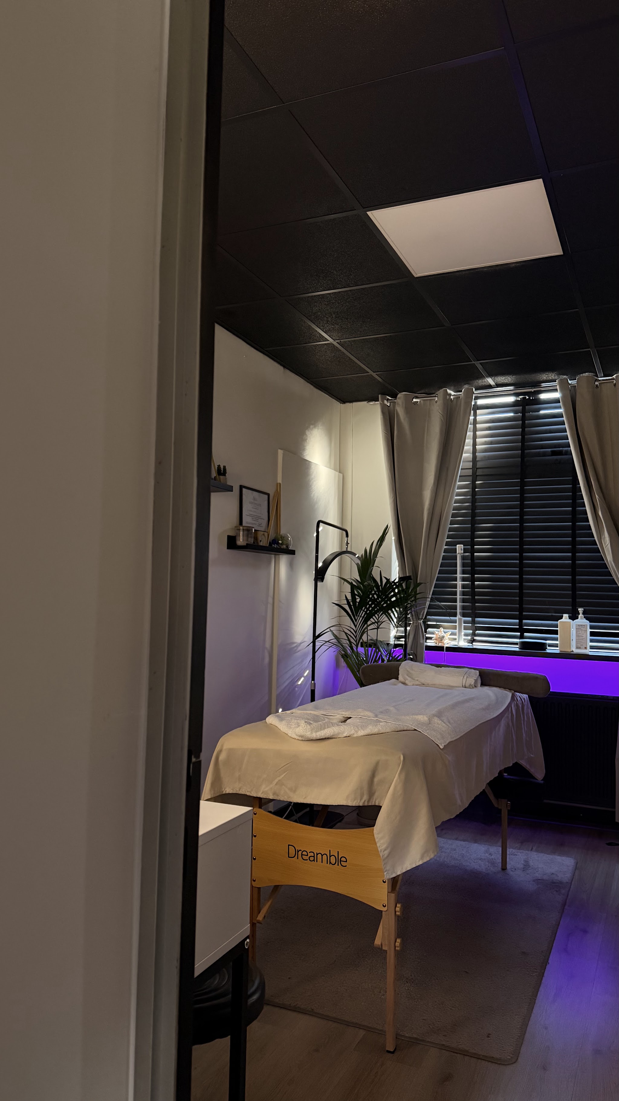 De massageruimte met een behandelbed, donker plafond en lamellen voor het raam